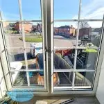 Interior cleaning of top-floor window with traditional tools and clear view of sunlit street in Pontefract